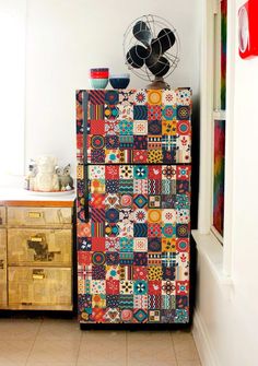 a multicolored refrigerator in a kitchen next to a cabinet with drawers and fan on top