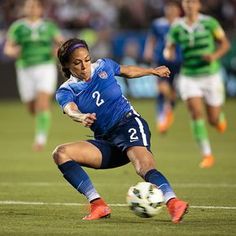 a woman kicking a soccer ball on top of a field