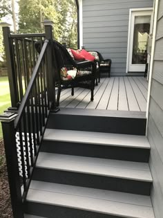 a deck with black railing and chairs on the front steps, next to a gray house