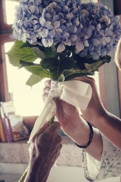 a woman holding a bouquet of blue flowers in her hands while another person places the ribbon on it