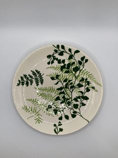 a white plate with green leaves and branches on the rim, against a gray background