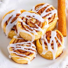 cinnamon rolls on a plate with icing drizzled over them and cinnamon sticks in the background