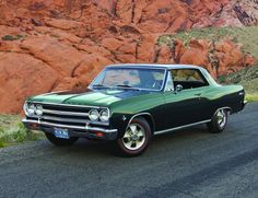 an old green and black car parked on the side of the road in front of some red rocks