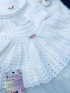 a white crocheted baby dress and booties are laying on a fur rug