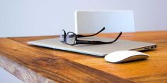 a laptop computer sitting on top of a wooden desk next to a pair of glasses