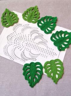 green crocheted leaves sitting on top of a piece of white paper next to a doily