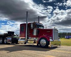 a red semi truck parked on the side of a road under a cloudy blue sky