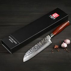 a large knife sitting next to some garlic and an open box on a wooden table