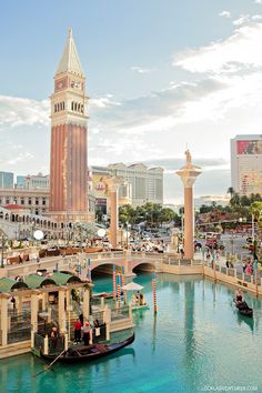 a boat floating down a river next to a tall building with a clock on it's side