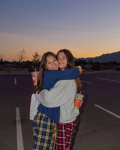 two girls hugging each other in the middle of a parking lot at sunset with mountains in the background