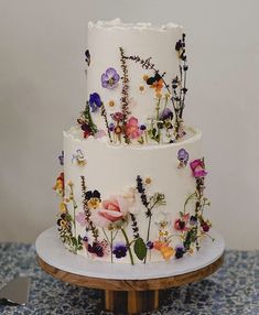 a three tiered cake decorated with flowers on a wooden stand next to a knife