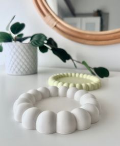 two white bracelets sitting on top of a table next to a plant and mirror