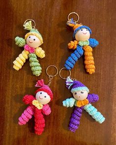 three crocheted dolls are hanging from key chains on a wooden table, one is wearing a hat and the other is holding a toy