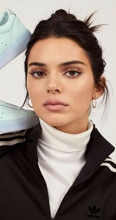 a woman is holding up her adidas sneakers in front of her face and looking at the camera