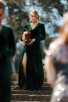 a woman in a green dress is walking down the stairs with flowers on her bouquet