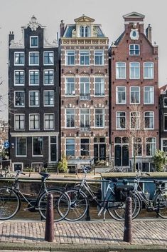 several bicycles parked next to each other on the side of a river with buildings in the background