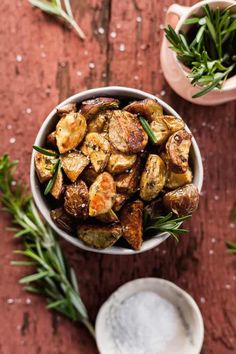 roasted potatoes in a bowl with rosemary sprigs on the side and two small dishes next to it