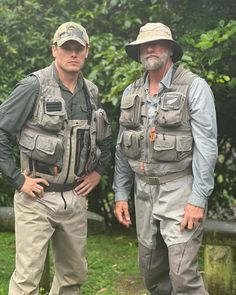 two men standing next to each other in front of trees