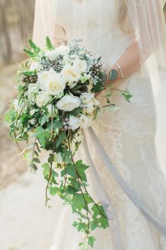 a bride holding a bouquet of white flowers and greenery