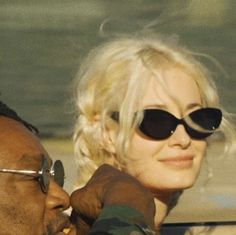 a man and woman sitting in the back seat of a car, both wearing sunglasses