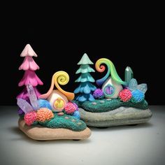 two small sculptures made out of clay with trees and rocks in the foreground on a black background