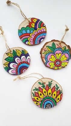 three wooden ornaments with colorful designs hanging from twine strings on a white table top