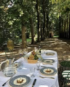 a table set with plates and silverware in the middle of a wooded area surrounded by trees