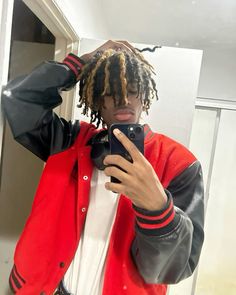 a man with dreadlocks is looking at his cell phone in the mirror while wearing a red jacket