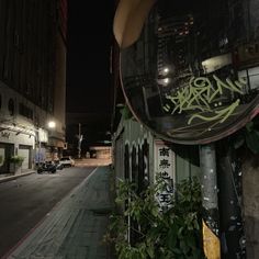 an empty city street at night with graffiti on the side of buildings and cars parked in front of it