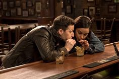 a man and woman sitting at a bar with drinks in front of their faces, one is biting into the other's mouth