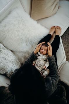 a woman holding a baby in her arms while sitting on a couch with white pillows