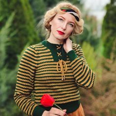 a woman holding a red rose in her right hand and wearing a green striped sweater