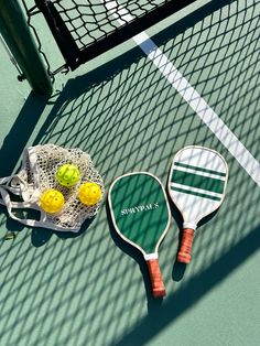 two tennis racquets and three balls on the ground next to a net