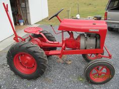 an old red tractor sitting in gravel next to a building