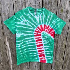 a green and red tie - dyed shirt hanging on a wooden fence