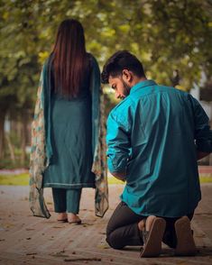 a man kneeling down next to a woman on the ground in front of some trees