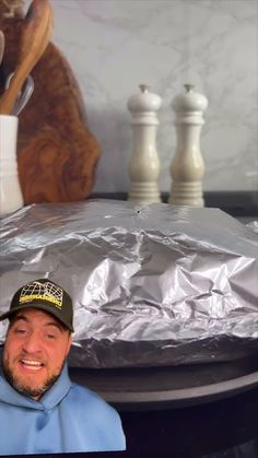 a man in a blue jacket and hat standing next to a table with silver foil on it