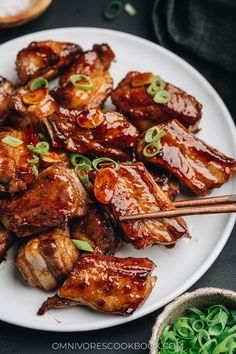 meat with chopsticks and sauce on a white plate next to some green vegetables