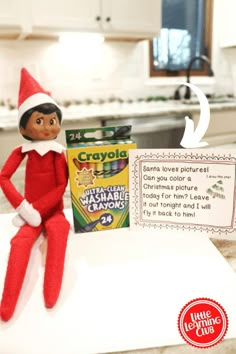 an elf is sitting on top of a box of crayola next to a sign