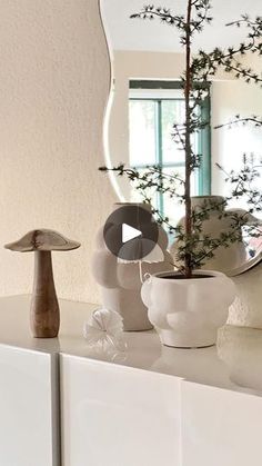 a white dresser topped with vases filled with flowers and trees in front of a mirror