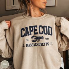 Show off your love of Cape Cod, one of the most iconic gems of Coastal Massachusetts with our custom Cape Cod Vacation Sweatshirt from Triangle Threads! Perfect for that Cape Cod Bachelorette Party or that Massachusetts family vacation, this crewneck features a vintage inspired design that highlights the lobster as one of Cape Cod's nautical and culinary traditions. The Gildan 18000 50/50 blend fabric has a comfy, lived-in feel that is perfect for hiking, camping, or wherever your day may take you. Grab yours today, and take a bit of the Cape with you wherever you wander! * Product Highlights * Ideal for any situation, this Gildan 18000 heavy blend crewneck sweatshirt is pure comfort. Made from an extremely soft 50/50 polyester and cotton blend, this combination helps keep you warm and com Cape Cod Bachelorette, Coastal Massachusetts, Cape Cod Travel, Varsity Crewneck, Cape Cod Vacation, Bachelorette Shirt, Travel Tees