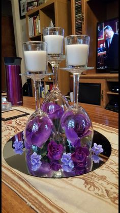 three wine glasses with flowers and candles on a table in front of a television set