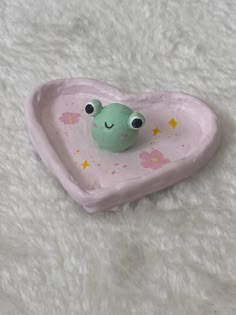 a pink heart shaped bowl with a green frog in it's center on a white surface