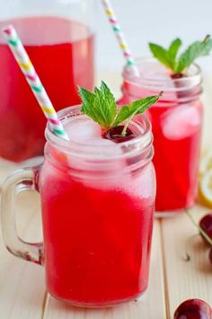 two mason jars filled with liquid and garnished with fresh mint leaves, surrounded by sliced lemons and cherries