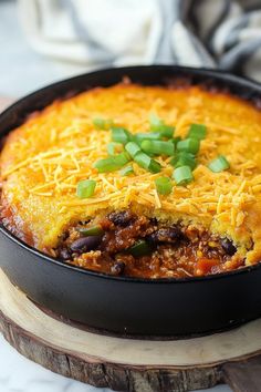 a skillet filled with chili and cheese on top of a wooden cutting board next to a fork