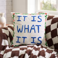 a pillow that says it is what it is sitting on a couch in front of a window