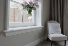 a white chair sitting in front of a window next to a vase filled with flowers