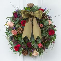 a wreath with flowers and pine cones hanging on a door