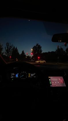 the dashboard of a car at night with traffic lights and trees in the back ground