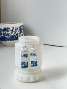 a pair of white and blue earrings sitting on top of a table next to a bowl